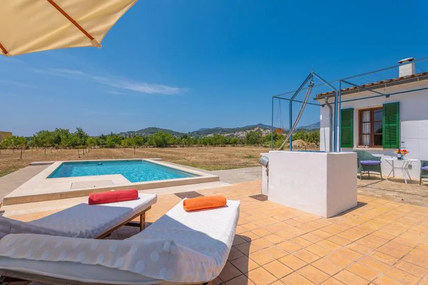 A sunny patio with a swimming pool, loungers, and a white building.