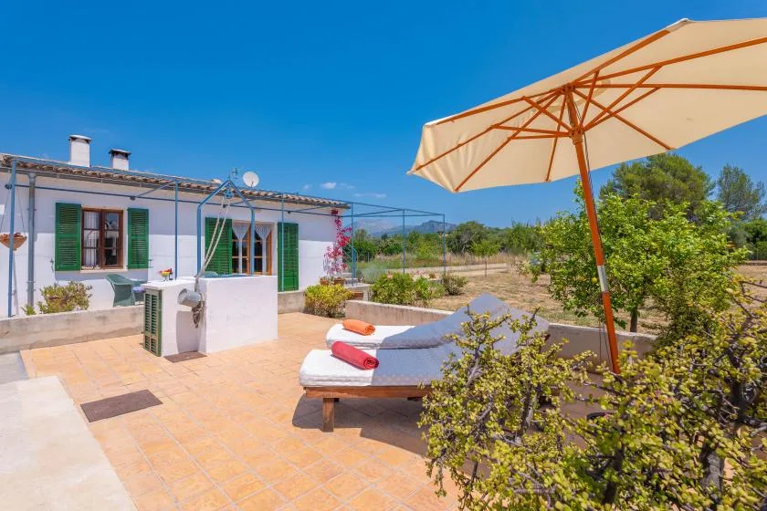 A sunny patio with cushioned seating, an open umbrella, and a white building.