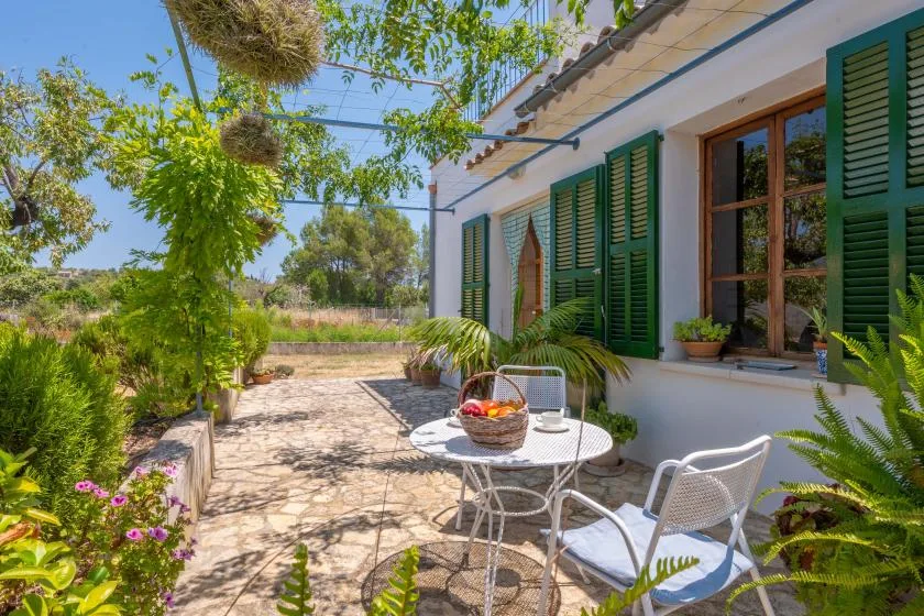 A sunny outdoor patio with a round table and green shutters along the house.