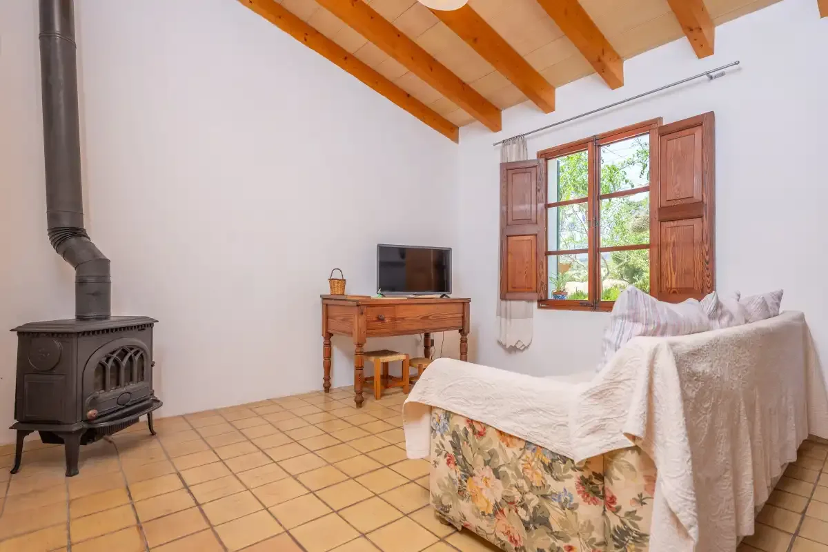 A bedroom with a bed, wooden ceiling beams, and a window with open shutters.