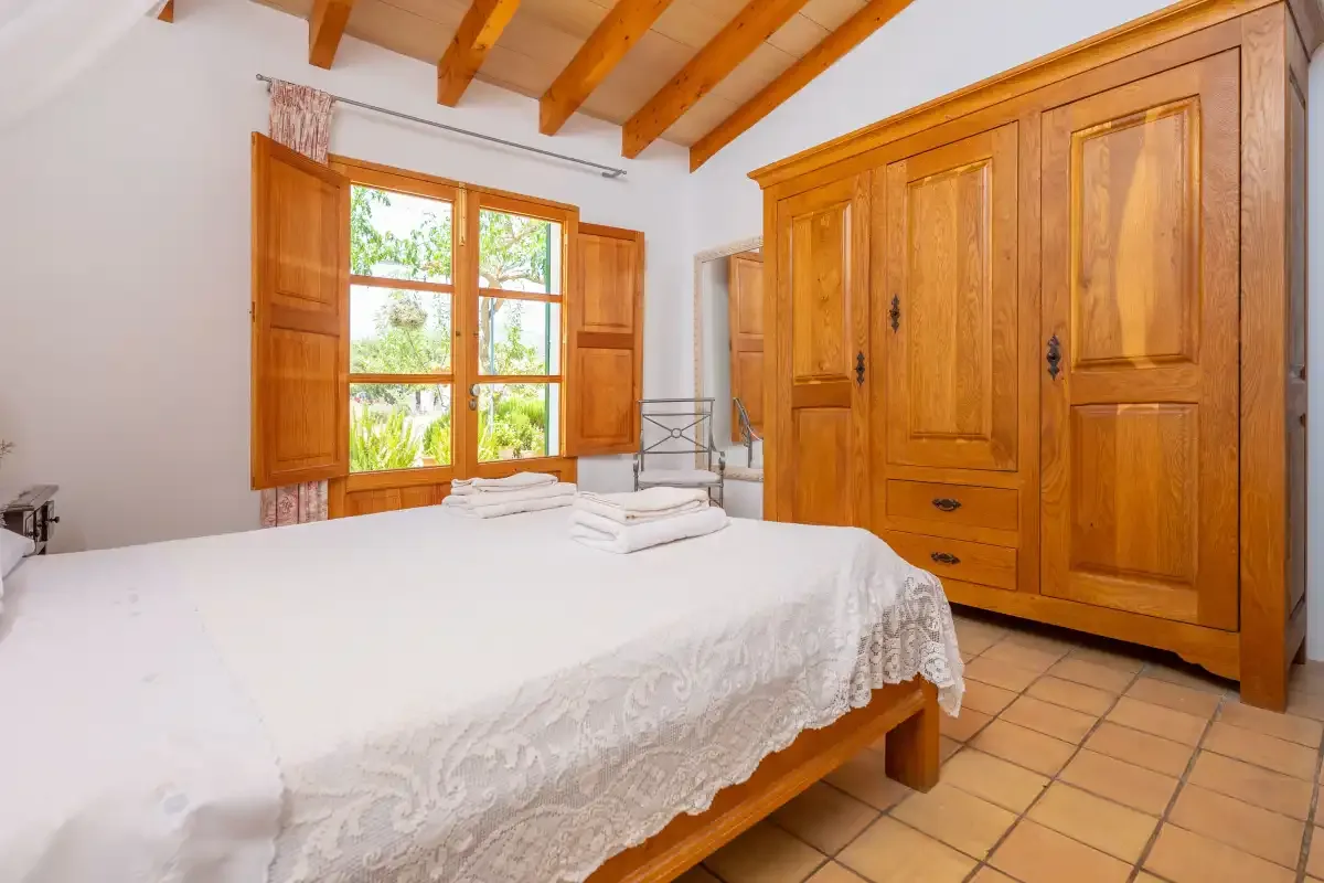 A bedroom with a large bed, wooden wardrobe, and window.