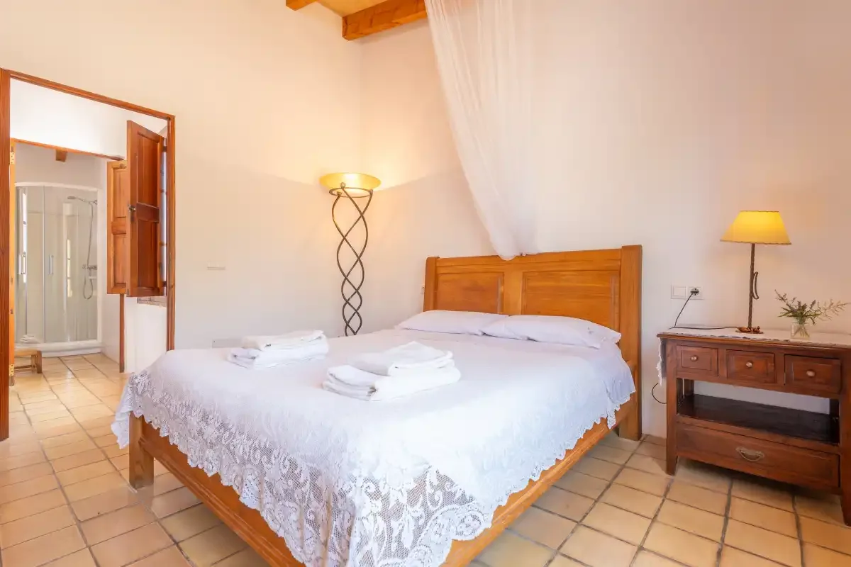 A bedroom with a wooden bed, white linens, and a tiled floor.