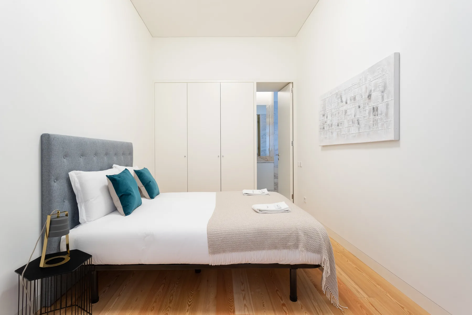 A bright bedroom with a neatly made bed and framed artwork.