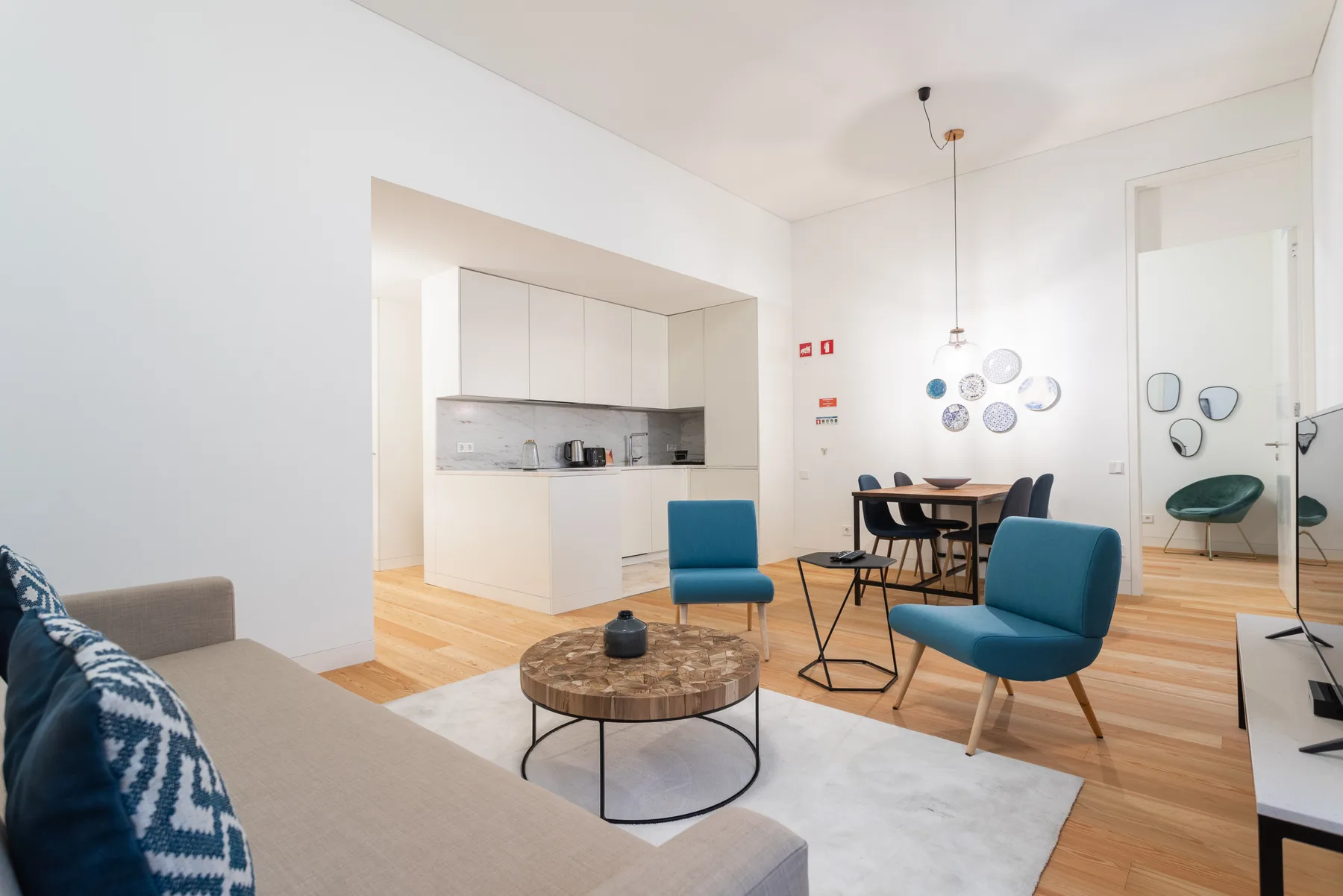 A bright living room with a kitchenette, blue seating, and a round coffee table.