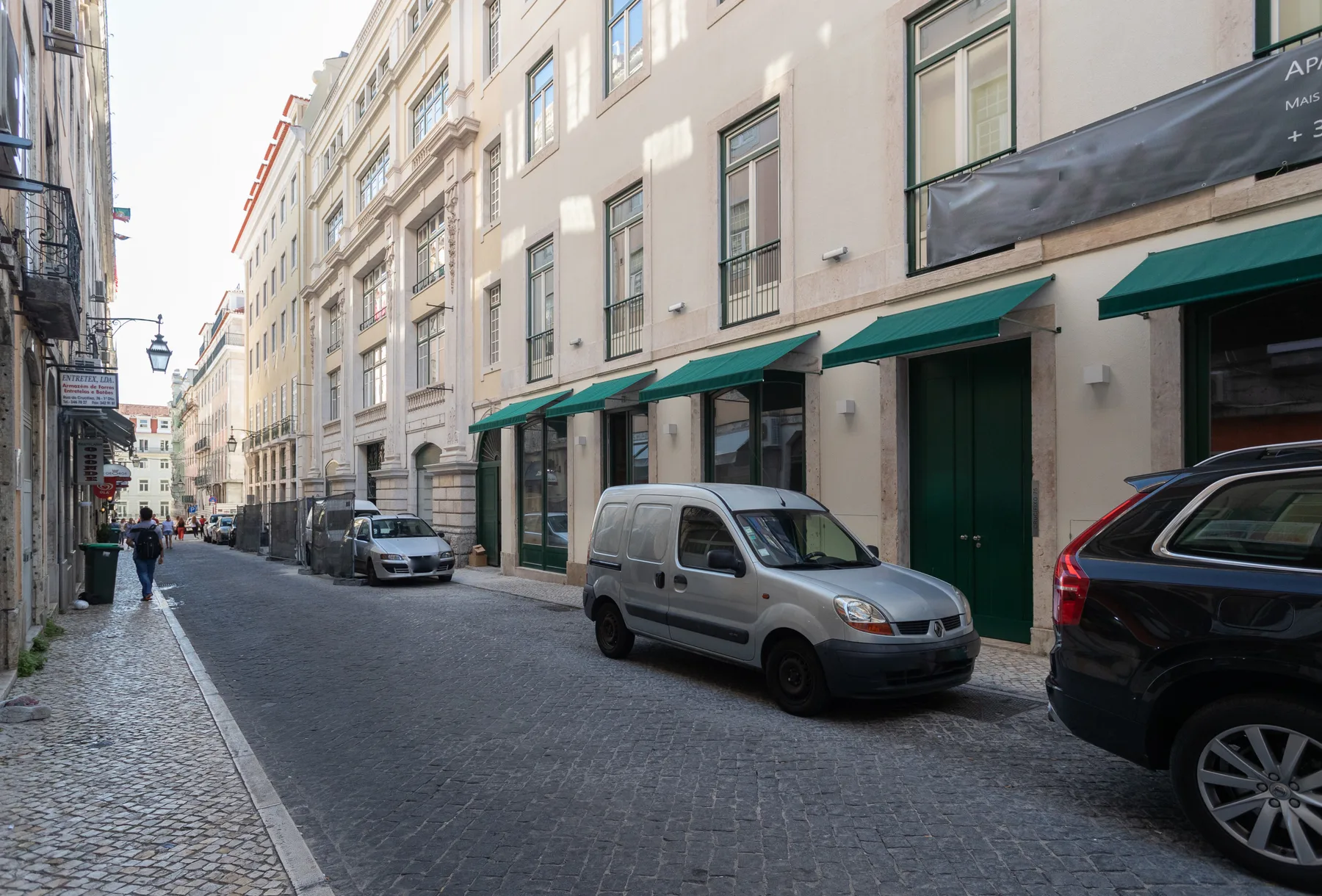 A narrow city street lined with tall buildings and parked vehicles.