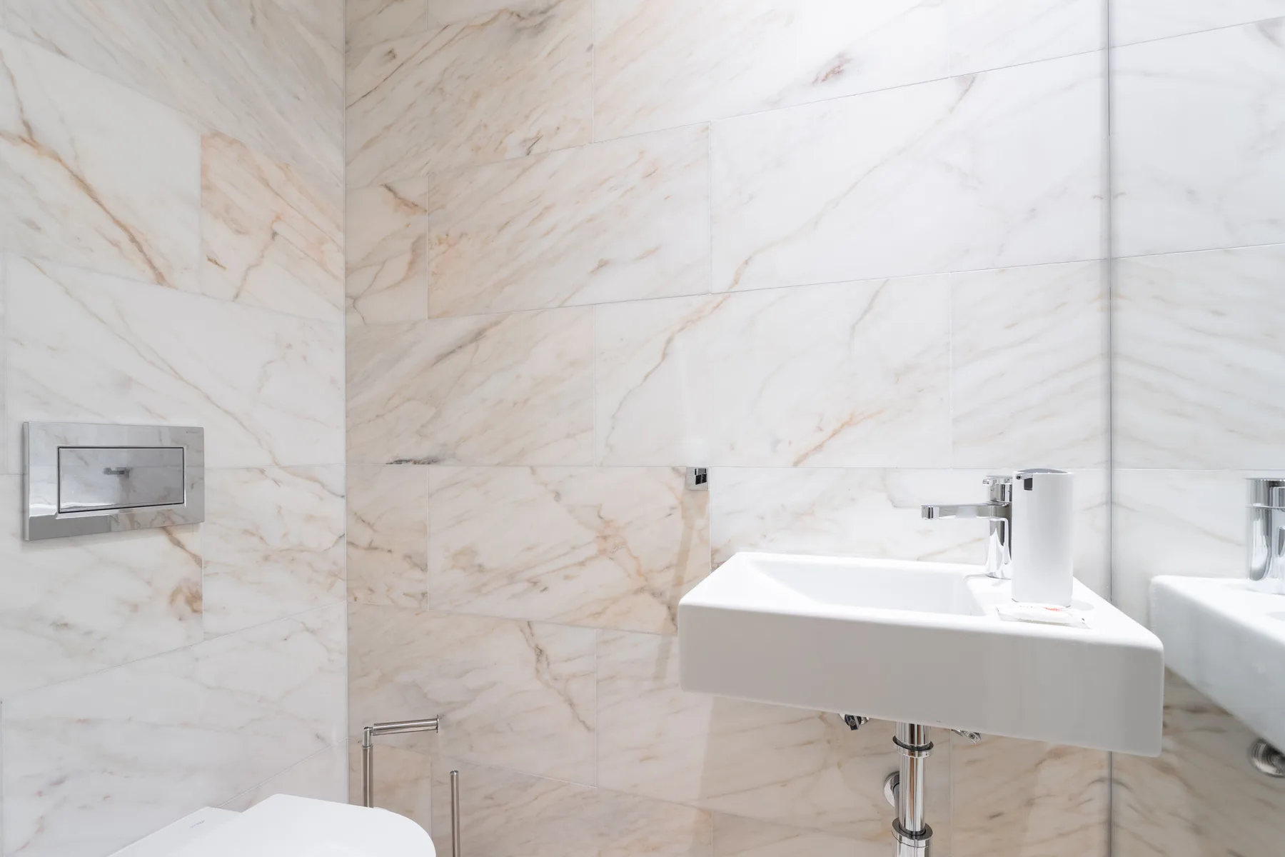 A bathroom with a wall-mounted sink and pale veined walls.