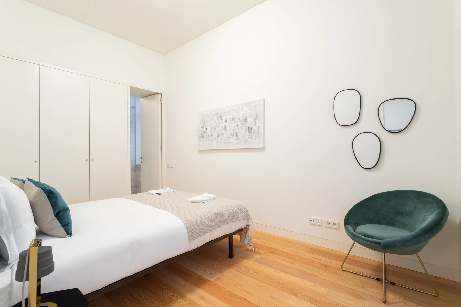 A bright bedroom with a bed, a green chair, and wall art.