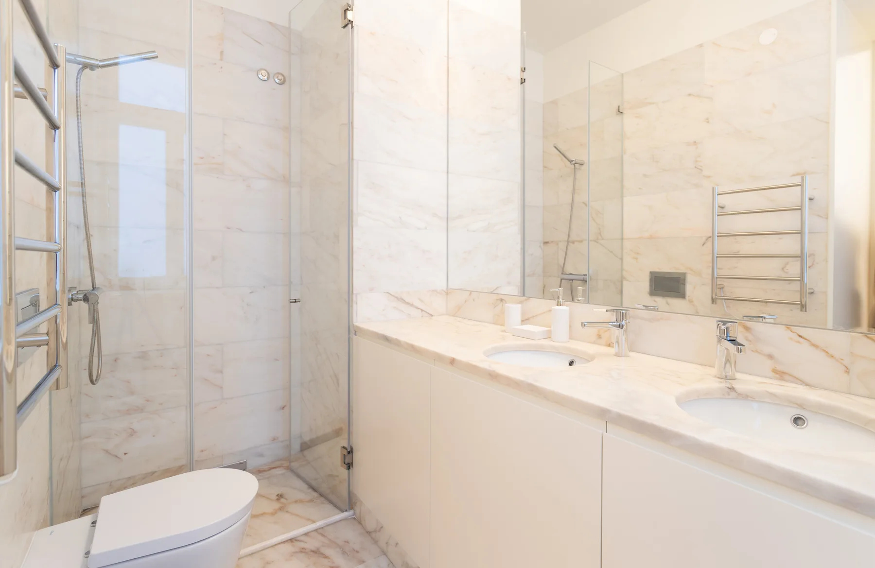 A bright bathroom with a glass shower and a long sink counter.