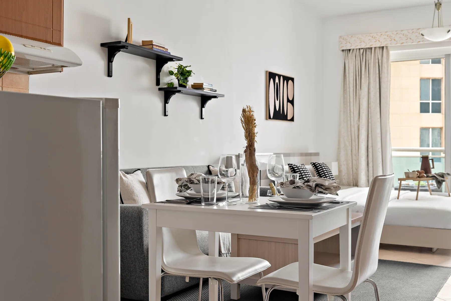 A dining table with place settings sits beside a living area and large window.