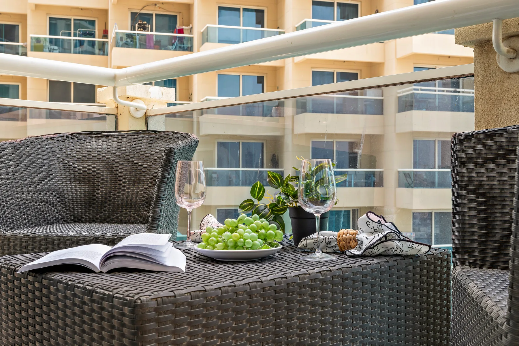 A balcony seating area with a table set with fruit, wine glasses, and an open book.