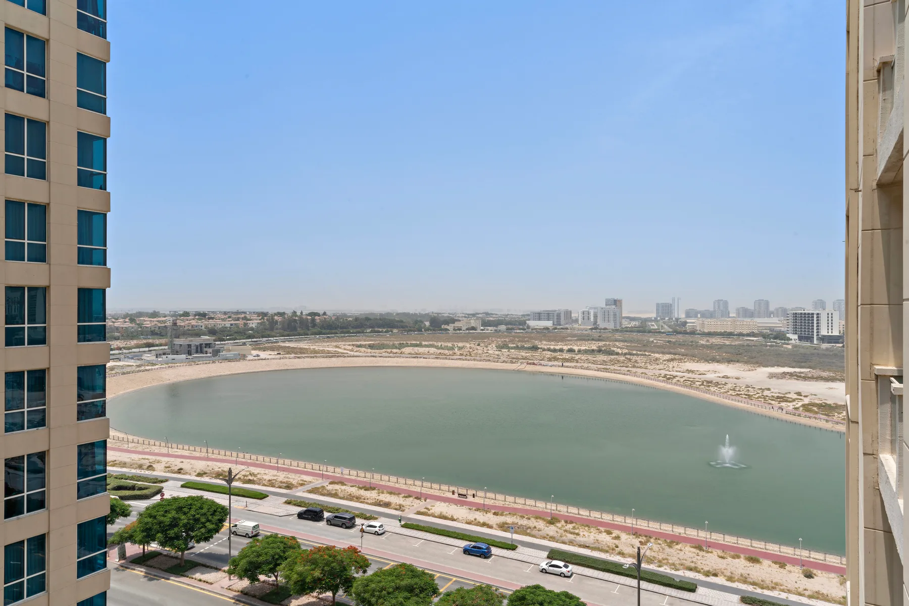 A city waterfront with a curved lagoon, a fountain, and buildings along the shore.