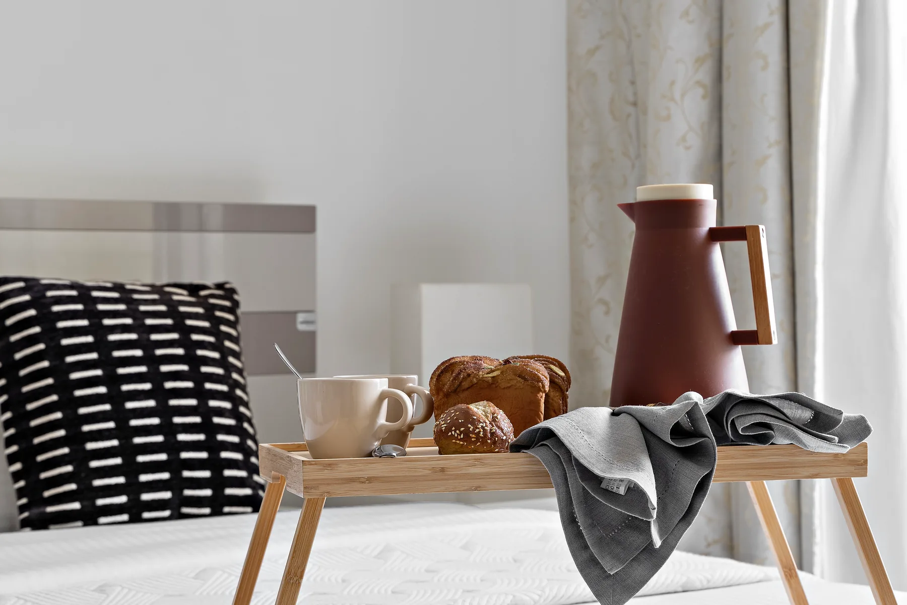 A bedroom scene with a tray holding coffee, bread, and folded clothing.