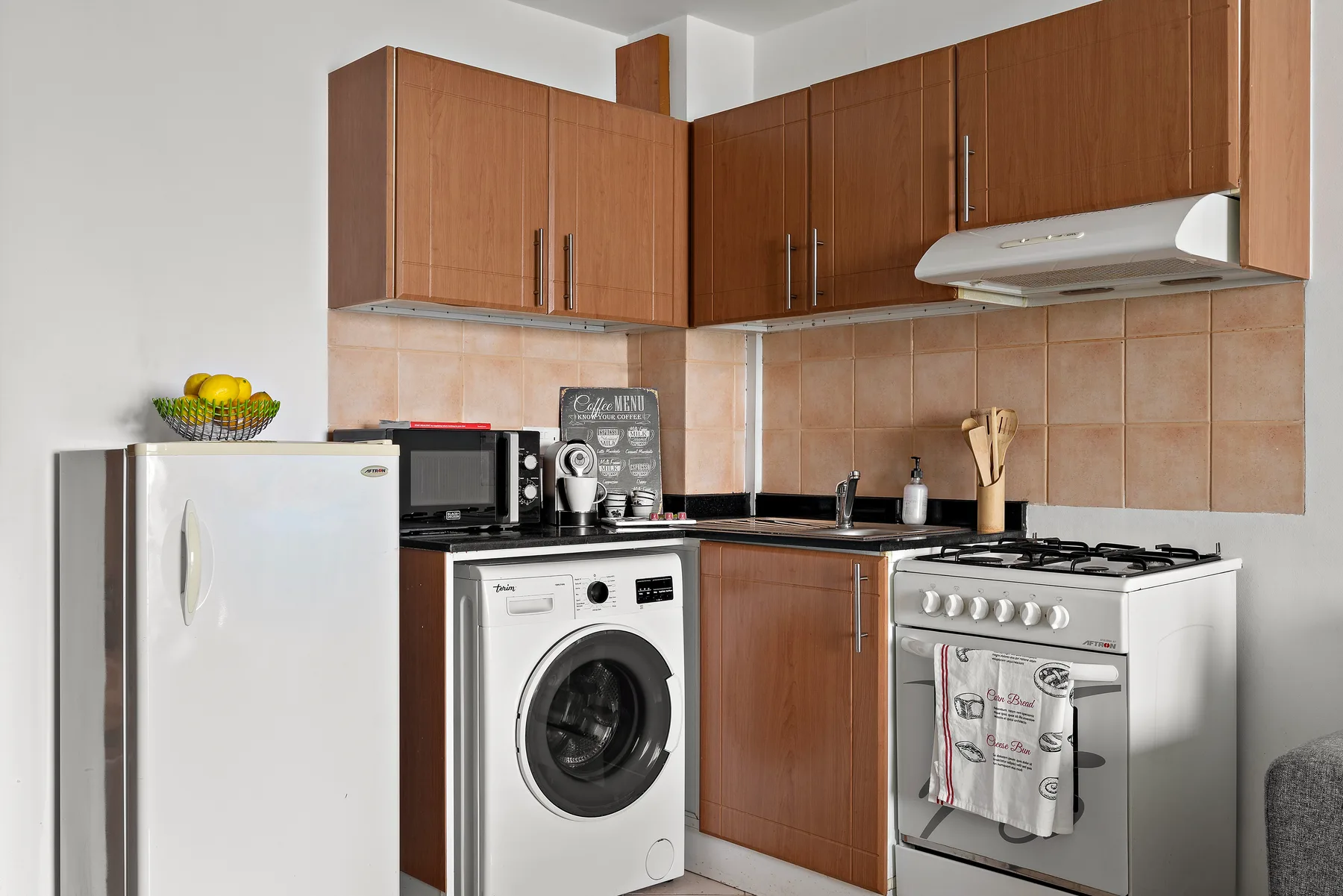 A compact kitchen with wooden cabinets, a washing machine, and a gas stove.