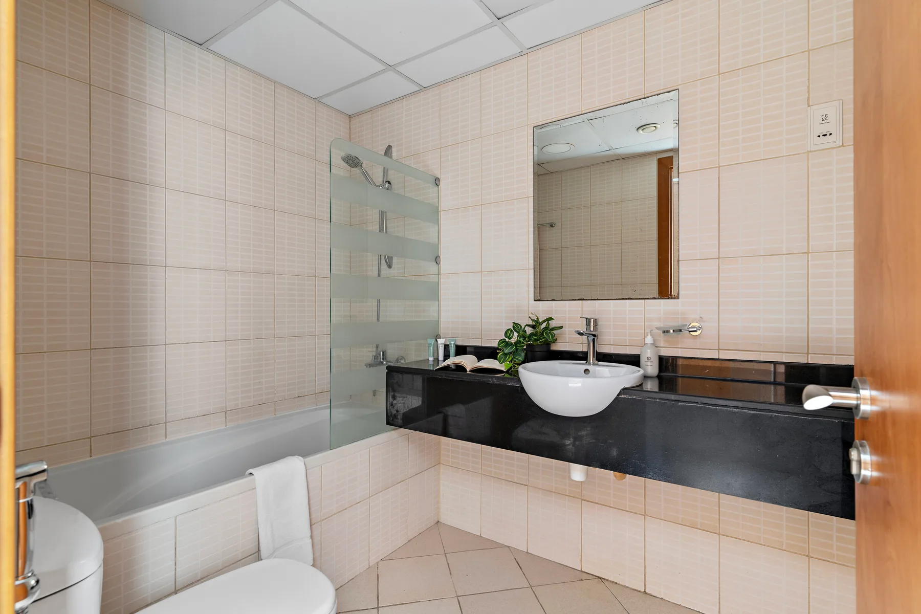A tiled bathroom with a bathtub, glass shower screen, and sink.