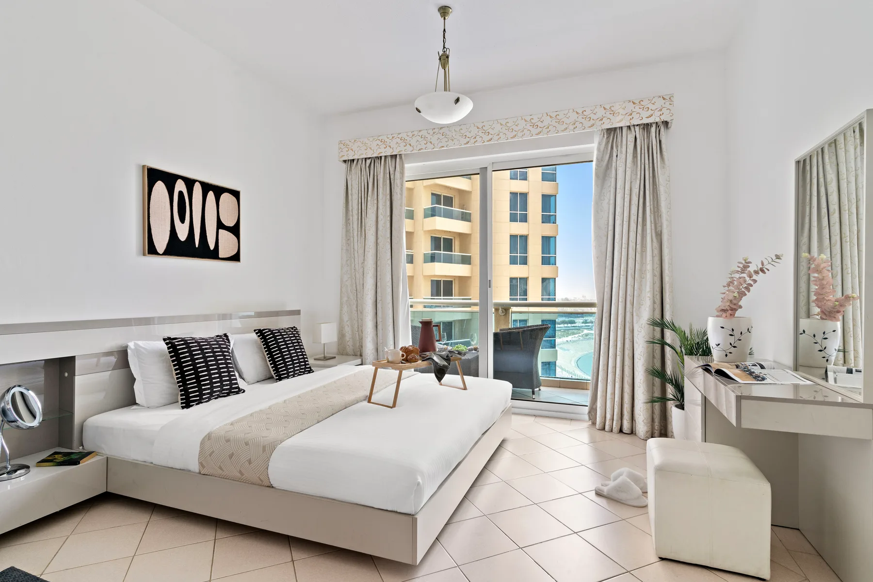 A bright bedroom with a large bed beside a sliding glass door and balcony.