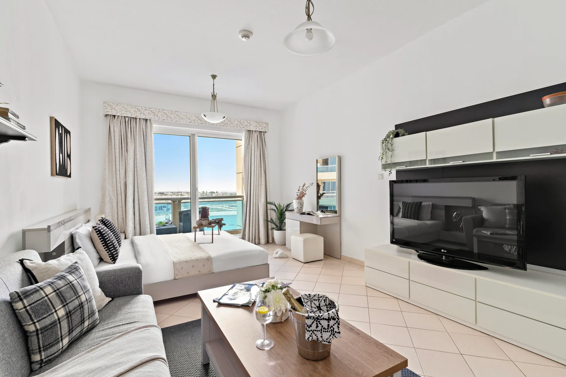 A bright living room with seating, a television, and a large window overlooking the water.