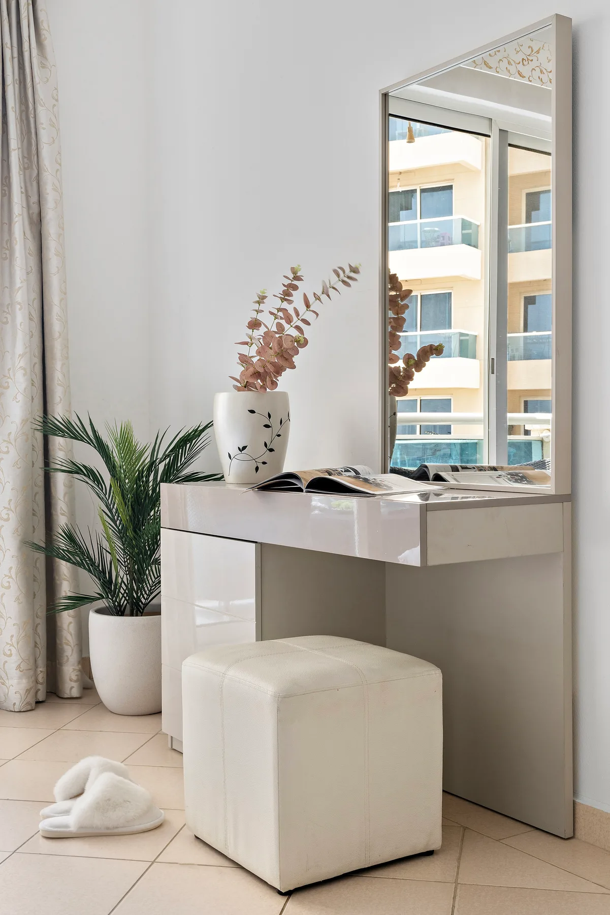 A bright vanity area with a mirror, padded stool, and potted plant.