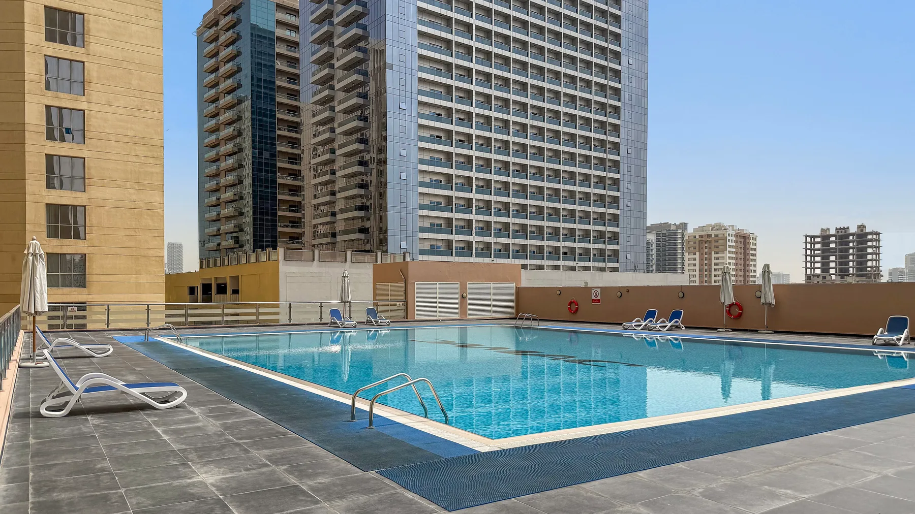 An outdoor swimming pool with lounge seating is surrounded by tall buildings.