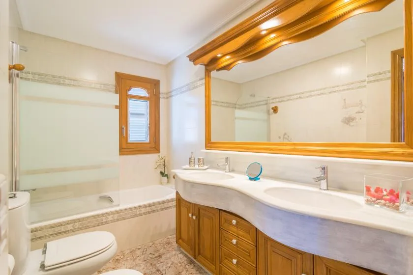 A bathroom with a bathtub, toilet, and long sink counter beneath a large mirror.