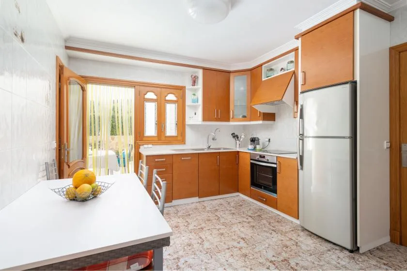A bright kitchen with wooden cabinets, a refrigerator, and a dining table.