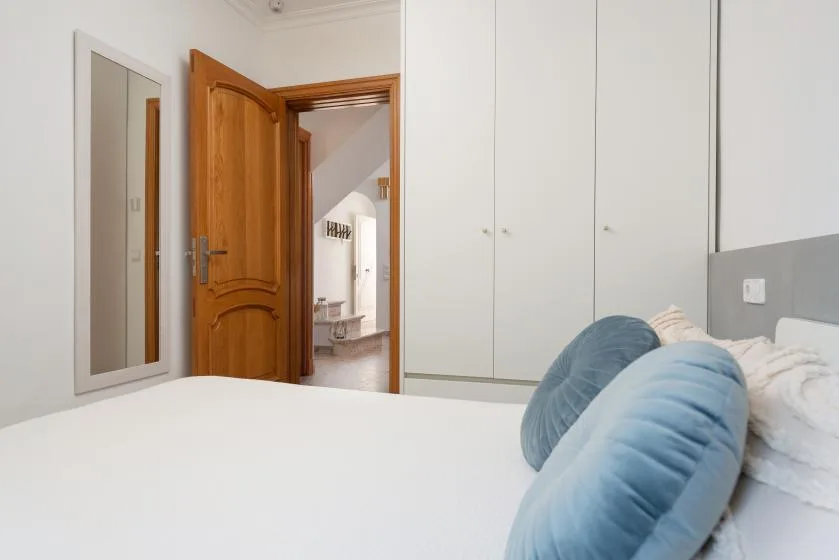 Bedroom with a white bed and blue cushions beside an open wooden door.