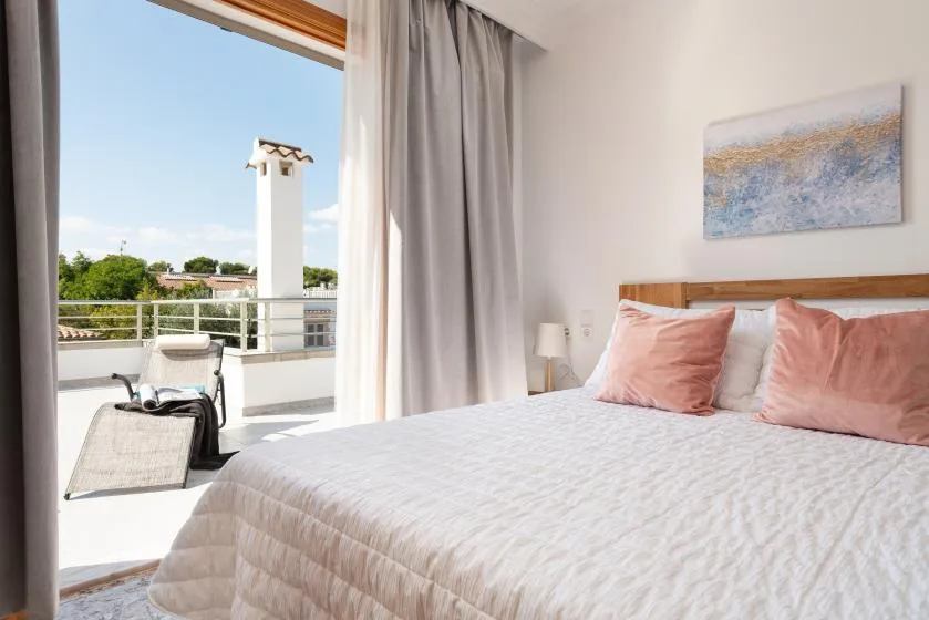 A bright bedroom with a bed beside an open balcony.