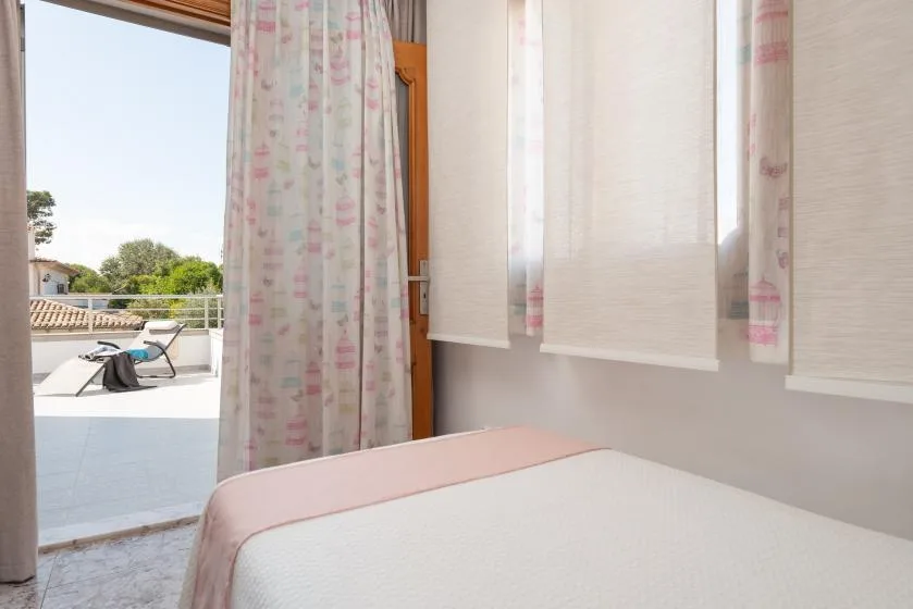 A bedroom with a bed beside a curtained glass door opening onto a terrace.