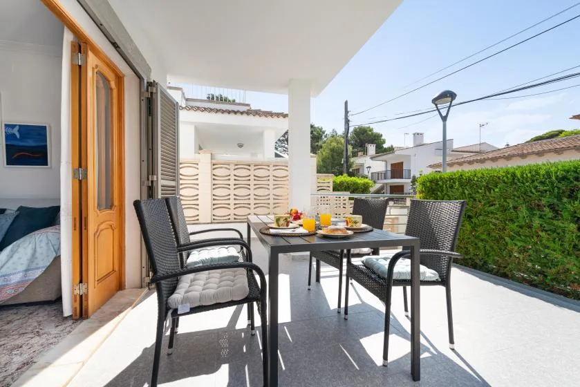 A covered outdoor patio has a dining table and seating beside an open doorway.