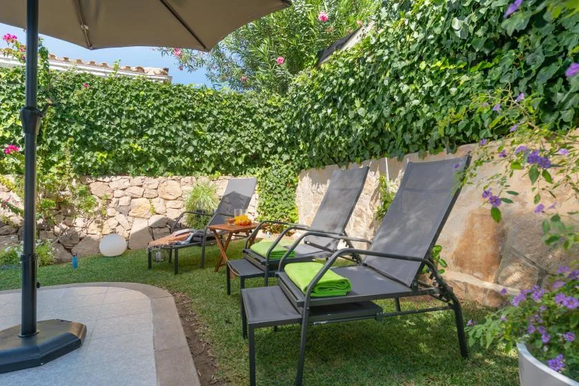 Outdoor seating area with reclining chairs beside a stone wall covered in greenery.