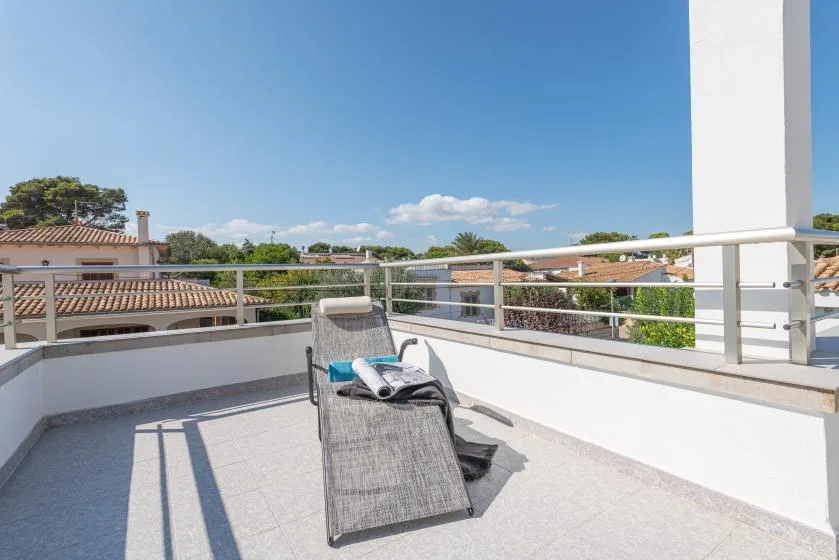 A sunny terrace with a reclining seat and railing overlooking nearby rooftops.
