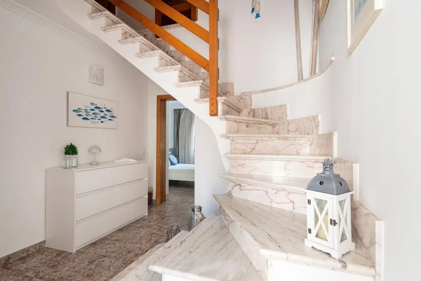 A curved staircase rises beside a white dresser in a bright interior.