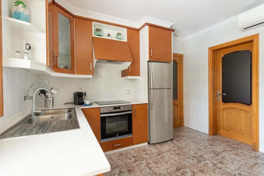 A compact kitchen with wood-toned cabinets, stainless steel appliances, and a tiled floor.