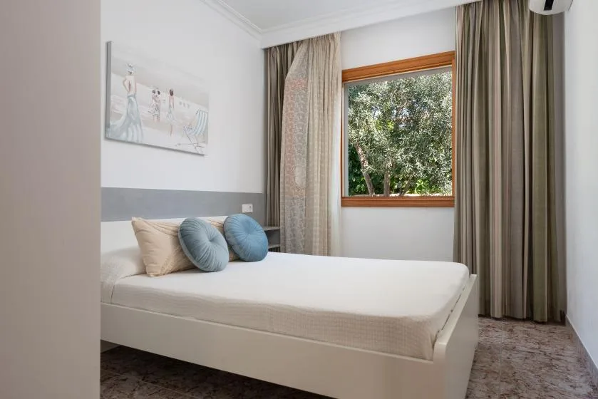 A bedroom with a neatly made bed, curtains, and a window overlooking trees.