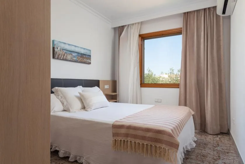 A bedroom with a neatly made bed and a window framed by curtains.