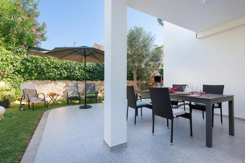 A covered outdoor dining patio with a table and seating beside a garden.