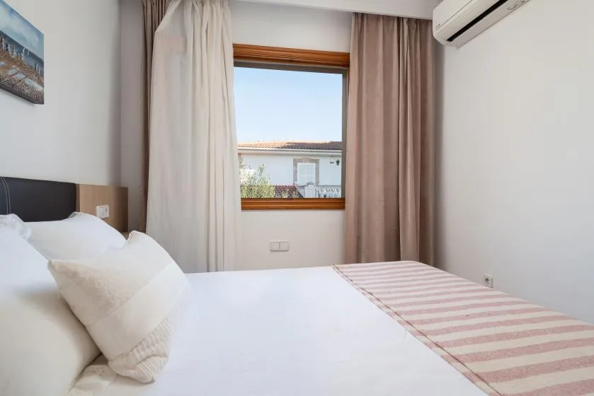 A bedroom with a neatly made bed beside a curtained window.