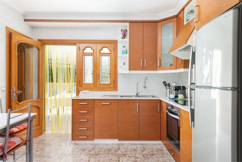 A bright kitchen with wooden cabinets, a window, and a large refrigerator.