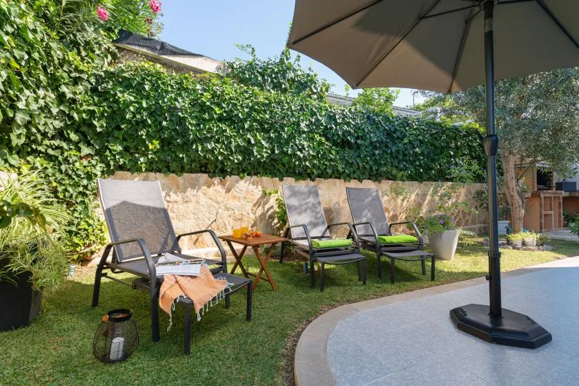 A garden seating area beside a curved patio, with lounge chairs and a large umbrella.
