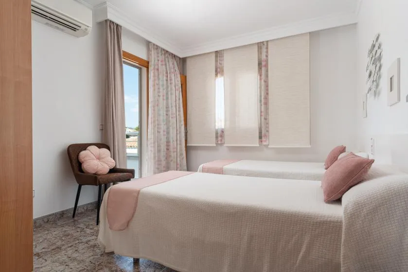 A bright bedroom with two beds, pale bedding, and floral curtains.