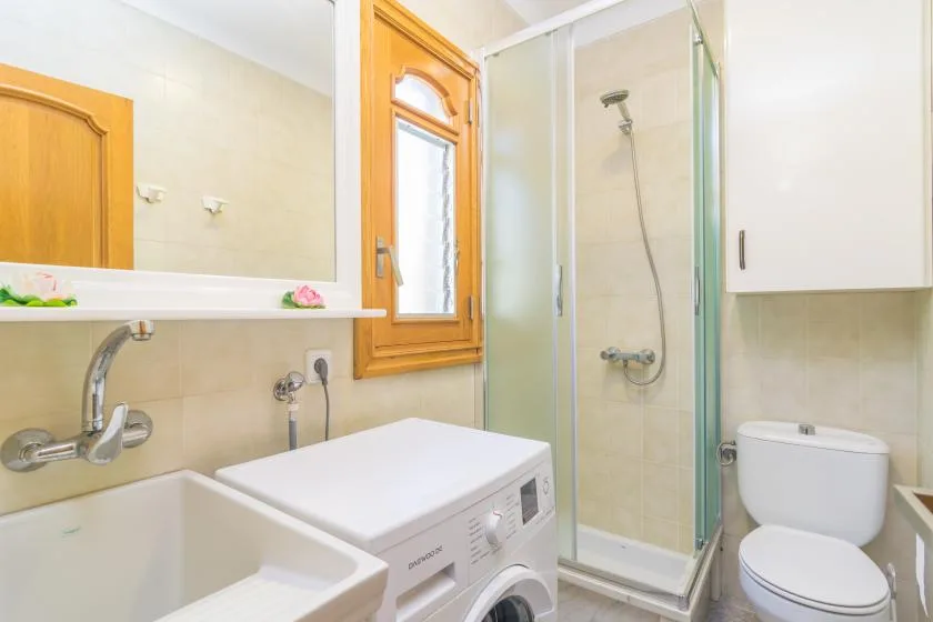 A bathroom with a sink, washing machine, toilet, and glass shower.