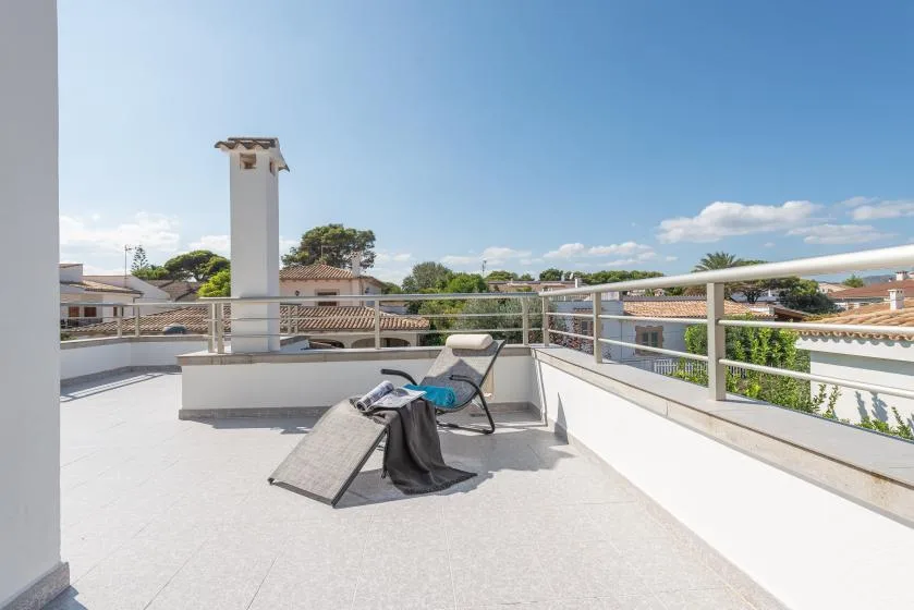 A sunny rooftop terrace has lounge seating and metal railings.