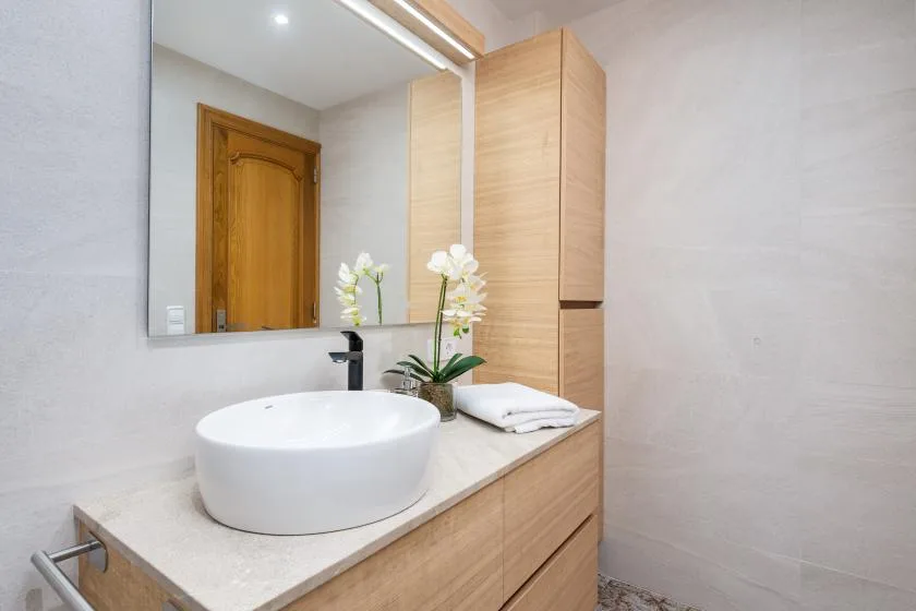 A bathroom vanity features a white vessel sink, mirror, and wooden cabinetry.