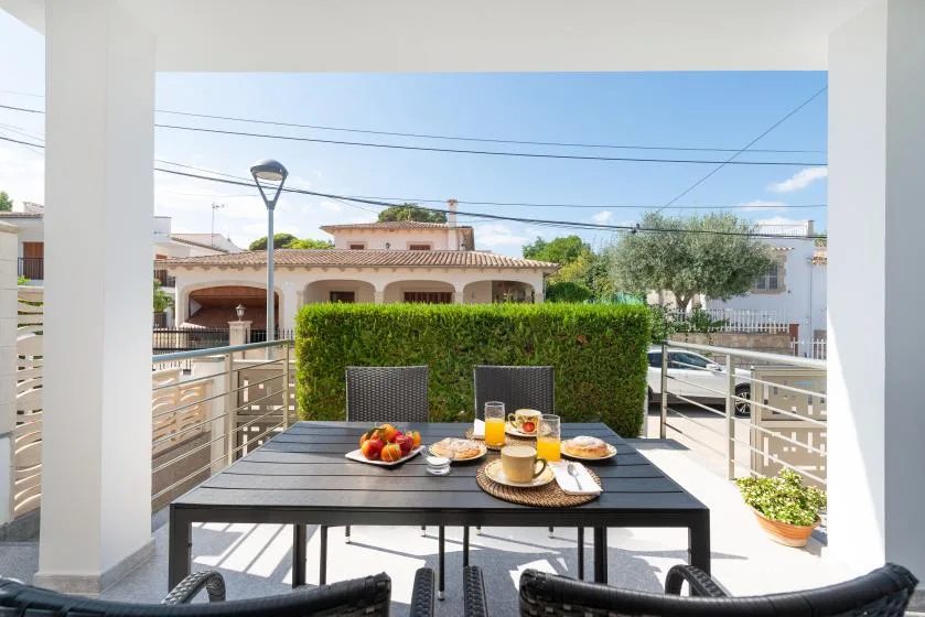 An outdoor dining area with a table set with food beside a green hedge.