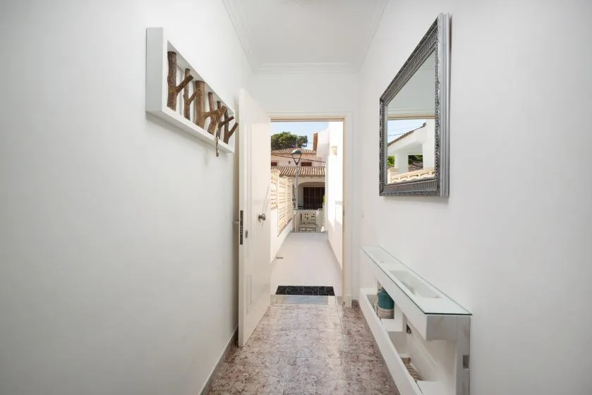 A narrow white hallway leads to an open doorway, with a glass-topped console along the wall.