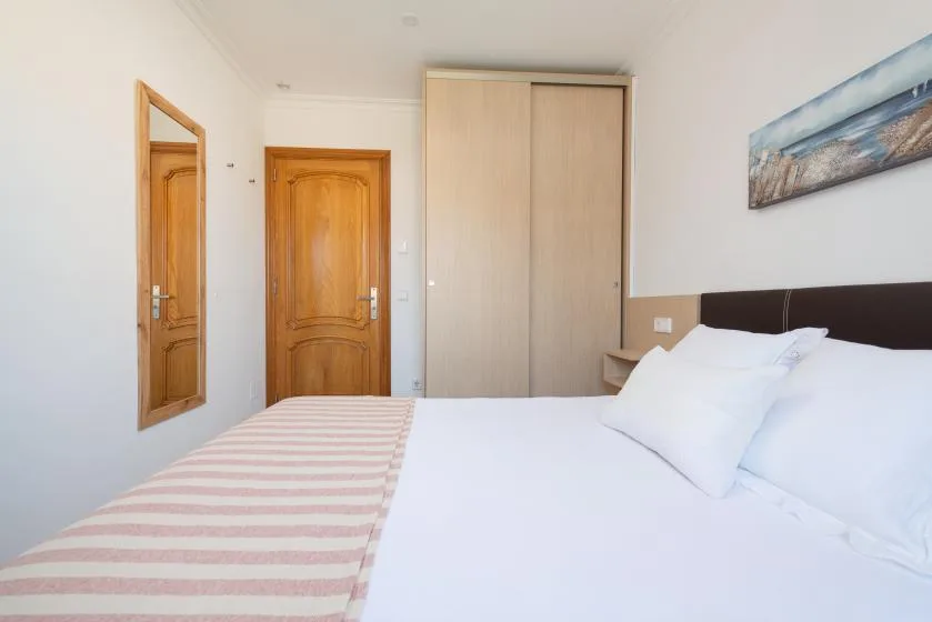 A bedroom with a bed, striped blanket, wardrobe, and wooden doors.