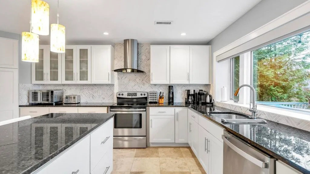 Una cocina luminosa con gabinetes blancos, encimeras oscuras y una ventana amplia.