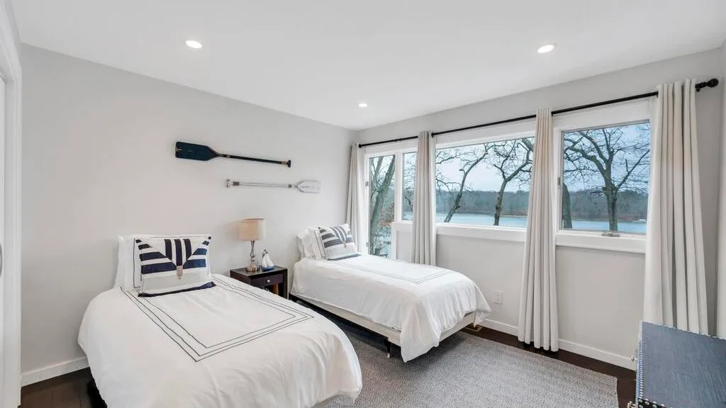 Un dormitorio luminoso con dos camas y grandes ventanas con vistas al agua.