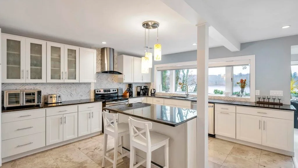 Una cocina luminosa con gabinetes blancos y una isla central con asientos.