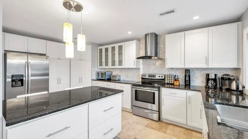 Una cocina luminosa con gabinetes blancos, electrodomésticos de acero inoxidable y una isla central.