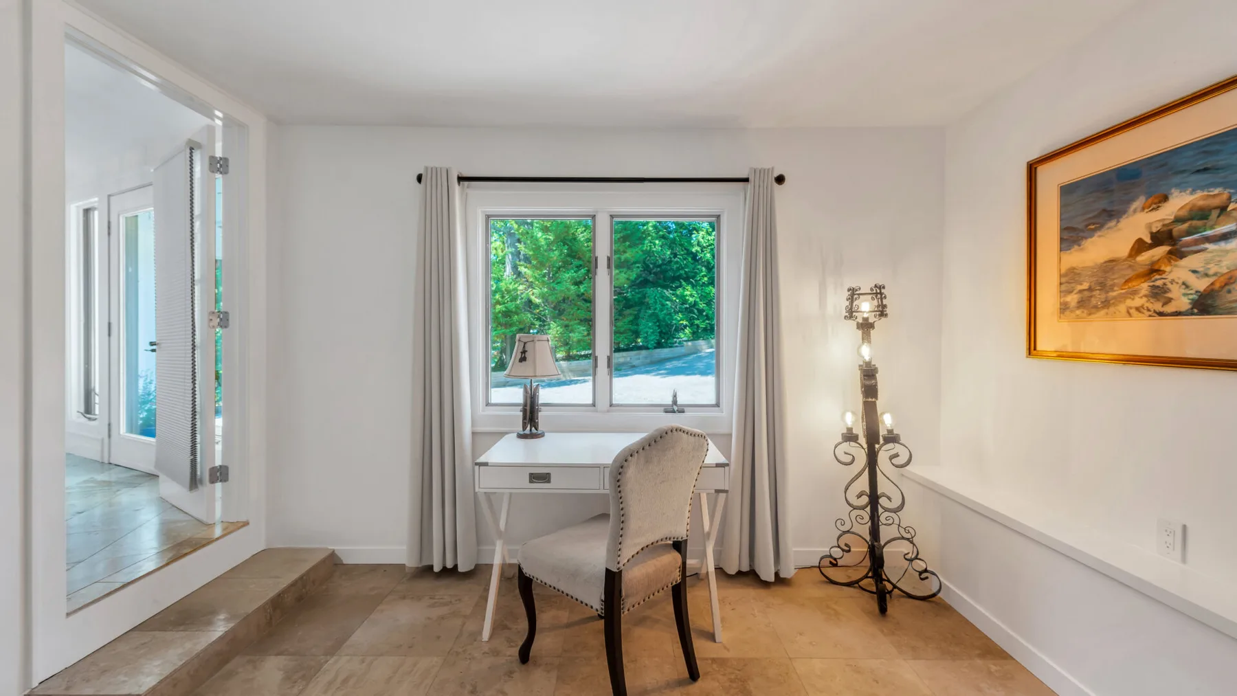 Una luminosa zona de estar con escritorio y una ventana con vistas a la vegetación.